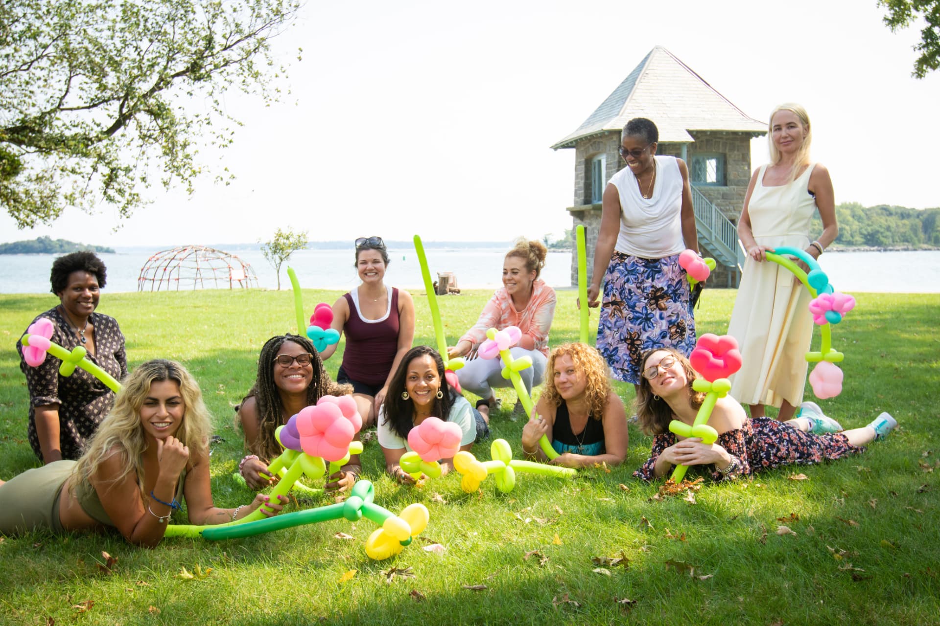 Women smiling together on the lawn by the water holding balloon flowers