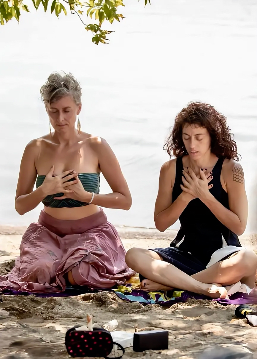 Two women meditating on a beach with hands on their hearts
